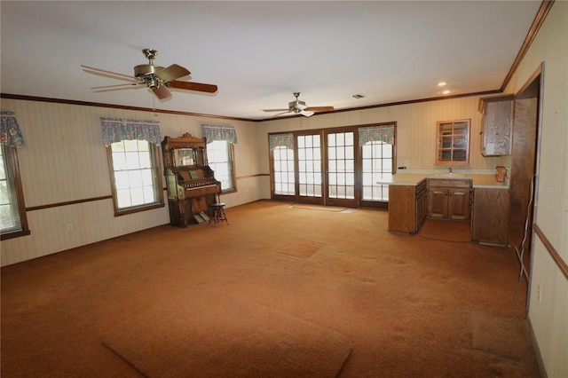 unfurnished living room with light carpet, a healthy amount of sunlight, ornamental molding, and ceiling fan