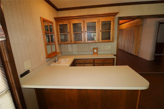 kitchen with wallpapered walls, light countertops, a sink, crown molding, and glass insert cabinets