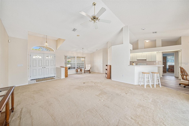 living room with ceiling fan with notable chandelier, high vaulted ceiling, a textured ceiling, and light colored carpet