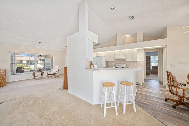 kitchen with light wood-type flooring, white appliances, a breakfast bar area, kitchen peninsula, and white cabinetry