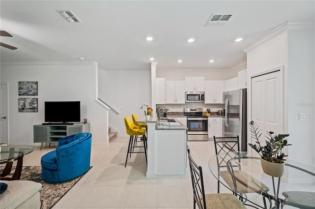 kitchen with dark stone countertops, white cabinets, ornamental molding, and stainless steel appliances