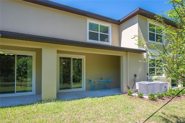 rear view of house with cooling unit, a lawn, and a patio