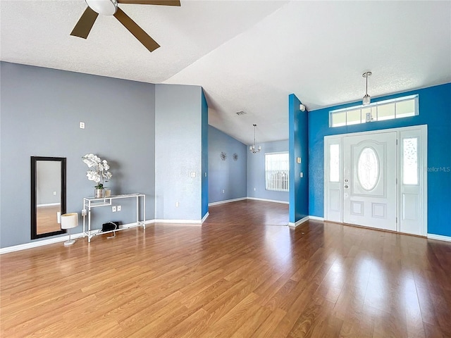 entryway featuring ceiling fan with notable chandelier, a textured ceiling, light wood-type flooring, and a wealth of natural light