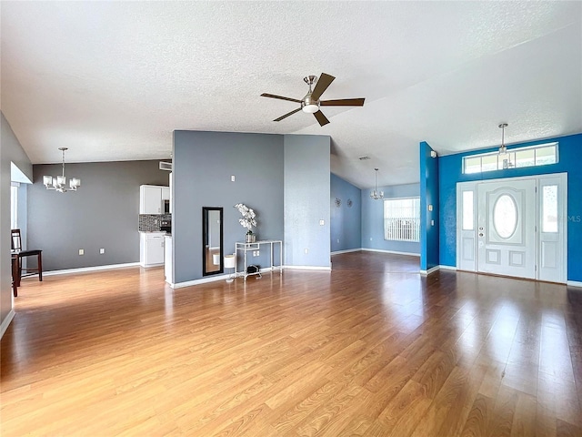 unfurnished living room with ceiling fan with notable chandelier, light wood-type flooring, a textured ceiling, and vaulted ceiling