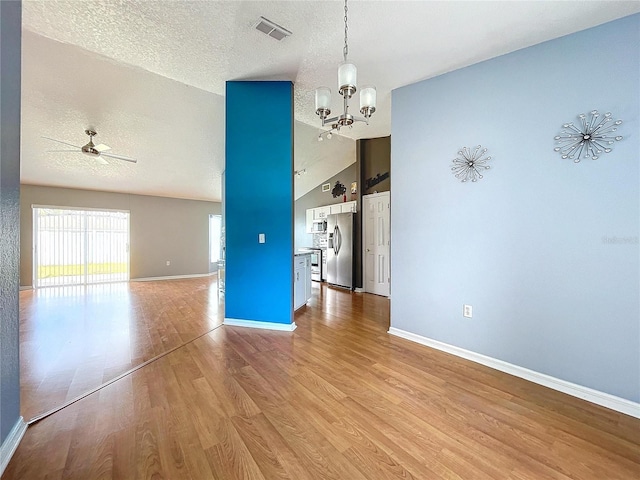 unfurnished dining area with ceiling fan with notable chandelier, a textured ceiling, light wood-type flooring, and vaulted ceiling