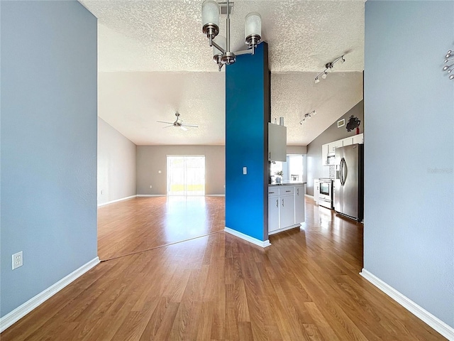 unfurnished living room featuring ceiling fan with notable chandelier, lofted ceiling, a textured ceiling, and light hardwood / wood-style flooring