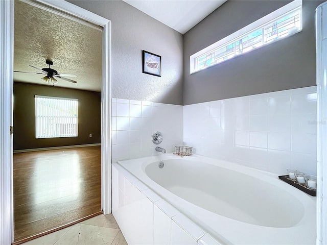 bathroom with tiled bath, ceiling fan, hardwood / wood-style floors, and a textured ceiling