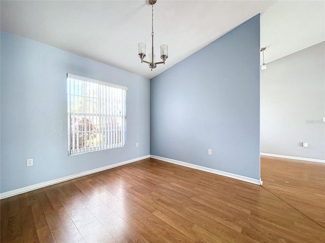 empty room with lofted ceiling, hardwood / wood-style flooring, and a notable chandelier