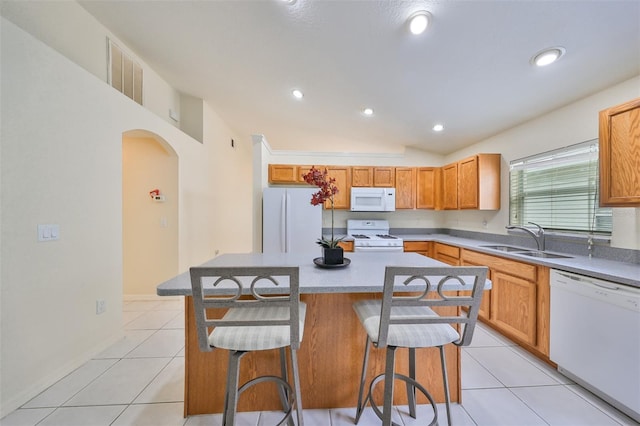 kitchen with white appliances, a center island, light tile patterned floors, a breakfast bar area, and sink