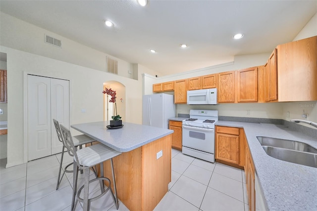 kitchen featuring white appliances, a center island, light tile patterned floors, a breakfast bar, and sink