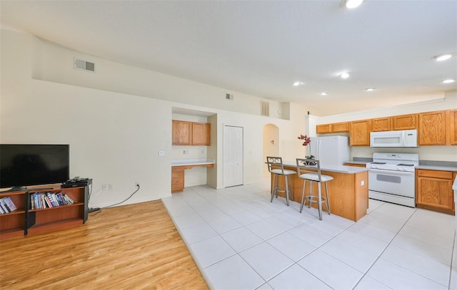 kitchen with a breakfast bar area, white appliances, a center island, and light tile patterned flooring