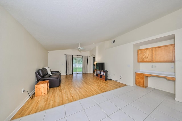 tiled living room featuring built in desk, ceiling fan, and vaulted ceiling