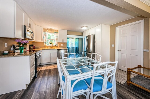 kitchen featuring white cabinets, a textured ceiling, stainless steel appliances, and dark wood-type flooring