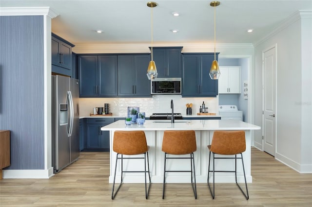 kitchen with sink, stainless steel appliances, hanging light fixtures, washer / clothes dryer, and an island with sink