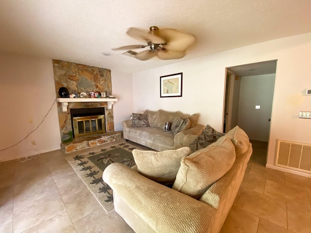 living area with ceiling fan, a stone fireplace, a textured ceiling, and visible vents