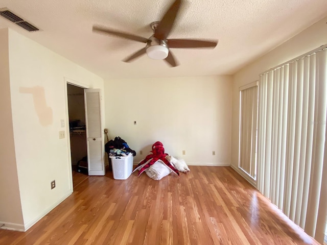 empty room featuring visible vents, light wood-style floors, a ceiling fan, a textured ceiling, and baseboards