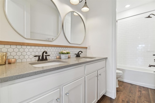 full bathroom featuring backsplash, hardwood / wood-style flooring, toilet, vanity, and tiled shower / bath combo