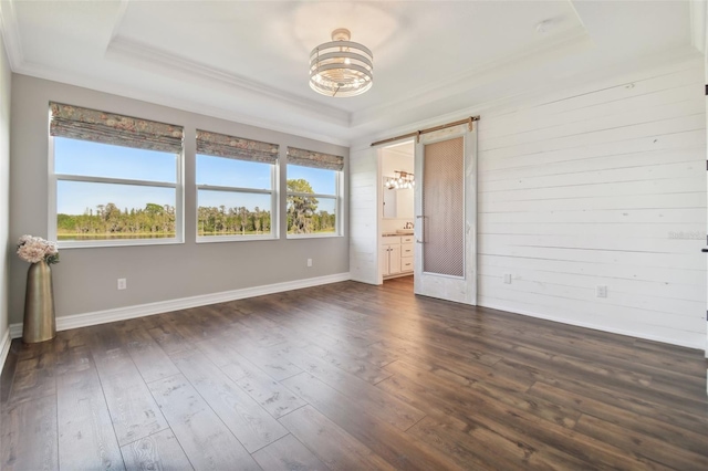 unfurnished room with a barn door, a raised ceiling, dark hardwood / wood-style flooring, wooden walls, and ornamental molding