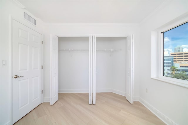 unfurnished bedroom featuring crown molding, light hardwood / wood-style flooring, and two closets