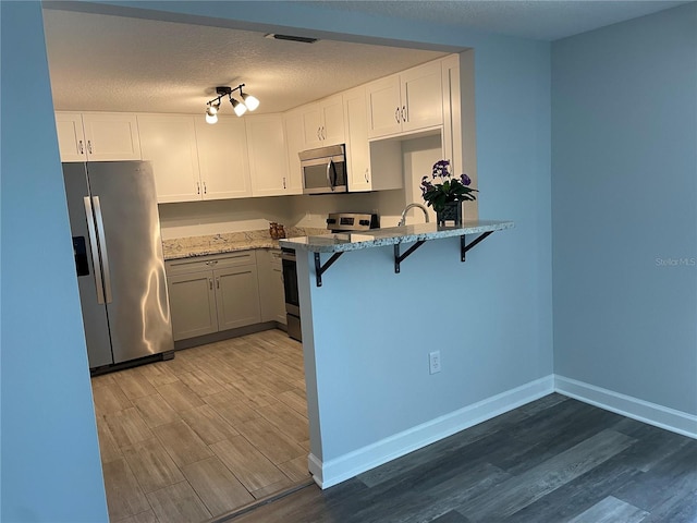 kitchen with light stone counters, wood-type flooring, a textured ceiling, white cabinetry, and stainless steel appliances