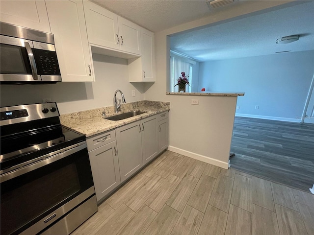 kitchen with sink, a textured ceiling, light hardwood / wood-style flooring, white cabinetry, and stainless steel appliances