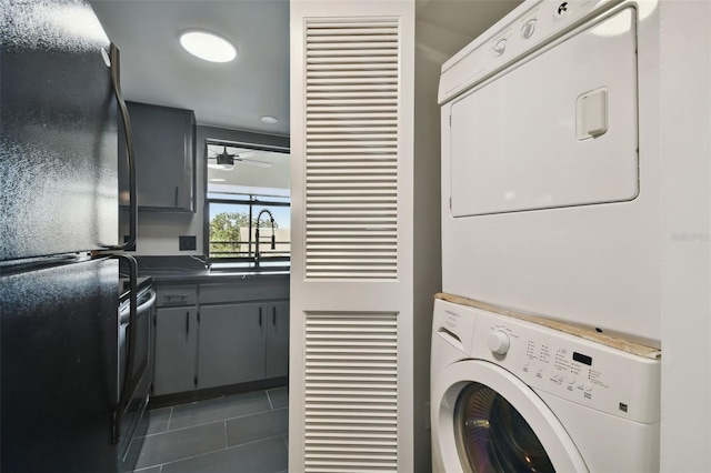 clothes washing area with ceiling fan, sink, dark tile patterned floors, and stacked washer and dryer