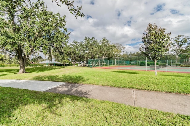 view of property's community featuring a lawn and tennis court