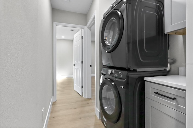 laundry room featuring cabinets, stacked washer and clothes dryer, and light wood-type flooring