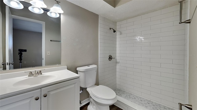 bathroom featuring a textured ceiling, tiled shower, toilet, a textured wall, and vanity