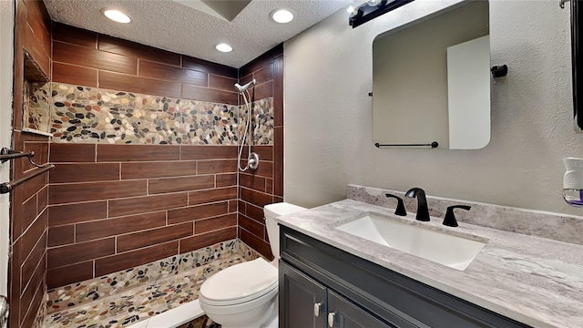 bathroom with a textured ceiling, vanity, a tile shower, toilet, and recessed lighting