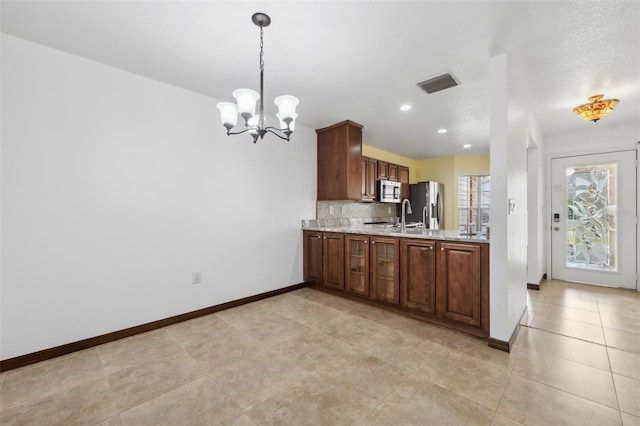 kitchen featuring decorative backsplash, hanging light fixtures, appliances with stainless steel finishes, a textured ceiling, and light stone countertops