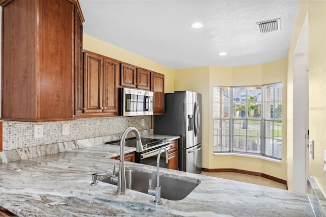 kitchen with decorative backsplash, light stone countertops, stainless steel appliances, and sink