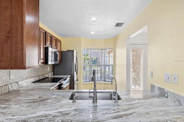 kitchen with decorative backsplash, appliances with stainless steel finishes, a textured ceiling, light stone countertops, and sink