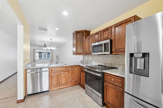 kitchen with stainless steel appliances, backsplash, sink, light stone countertops, and decorative light fixtures