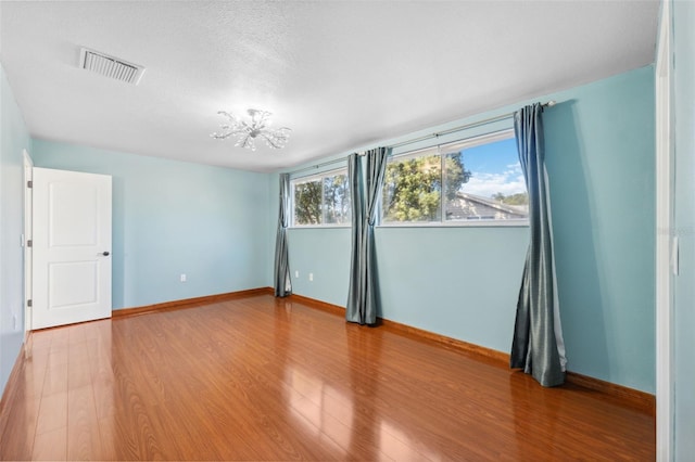 empty room with wood-type flooring, a textured ceiling, and a chandelier