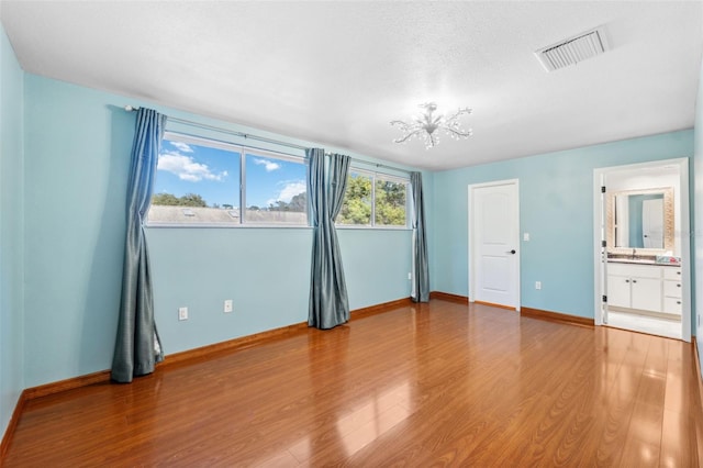 unfurnished bedroom with hardwood / wood-style floors, a textured ceiling, ensuite bathroom, a notable chandelier, and sink