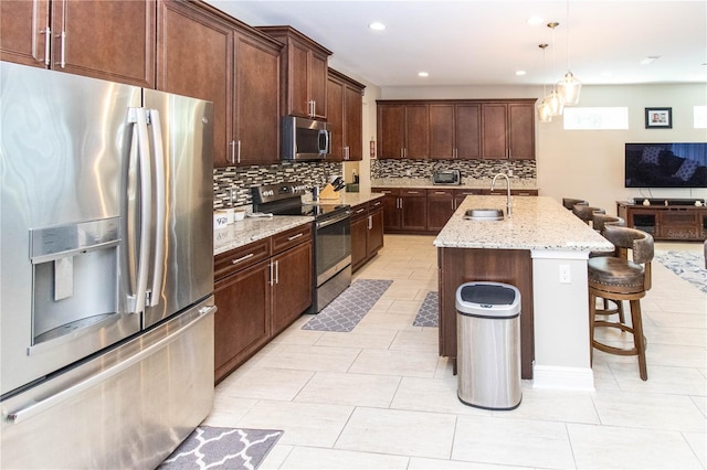 kitchen with a kitchen island with sink, sink, light stone countertops, decorative light fixtures, and appliances with stainless steel finishes