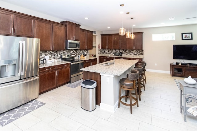 kitchen featuring stainless steel appliances, a center island with sink, sink, pendant lighting, and light stone counters