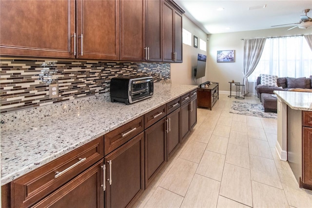 kitchen with ceiling fan, light stone counters, a healthy amount of sunlight, and tasteful backsplash