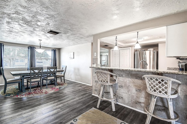 kitchen featuring dark wood-type flooring, stainless steel fridge, white cabinetry, hanging light fixtures, and light stone counters