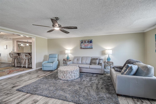 living room featuring hardwood / wood-style flooring, crown molding, ceiling fan, and a textured ceiling