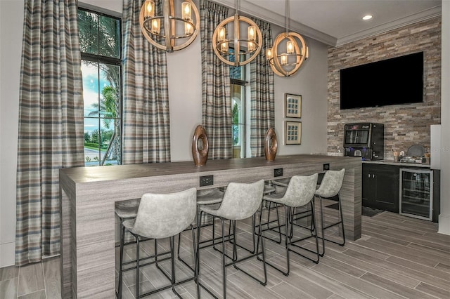 bar with beverage cooler, light wood-type flooring, crown molding, and hanging light fixtures