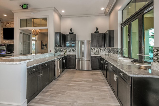kitchen featuring stainless steel appliances, light stone counters, a peninsula, ornamental molding, and a chandelier