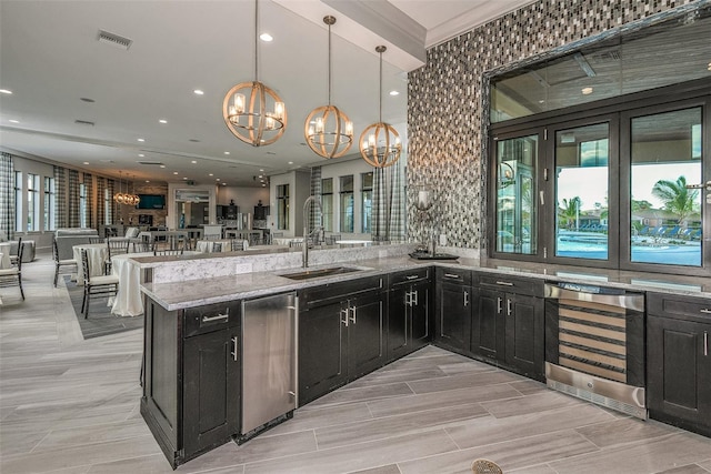 kitchen with an inviting chandelier, pendant lighting, beverage cooler, sink, and light stone countertops