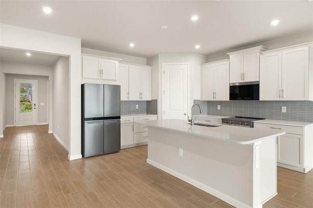 kitchen featuring stainless steel appliances, a sink, recessed lighting, light countertops, and a kitchen island with sink