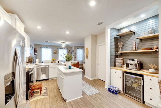 kitchen with beverage cooler, a kitchen island, appliances with stainless steel finishes, white cabinetry, and light hardwood / wood-style floors