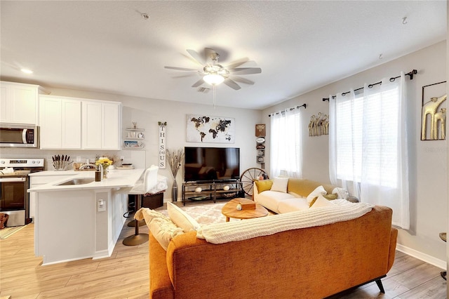 living room with sink, light wood-type flooring, and ceiling fan