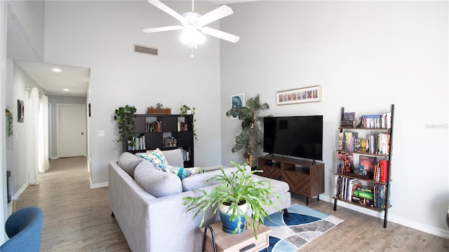 living room with ceiling fan, a towering ceiling, and light hardwood / wood-style floors