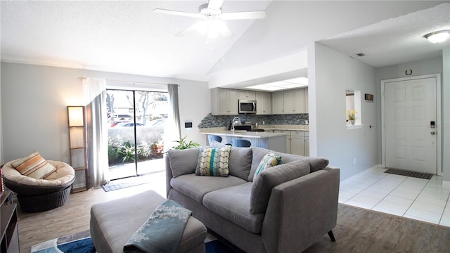 living room with ceiling fan, a textured ceiling, light hardwood / wood-style flooring, and vaulted ceiling