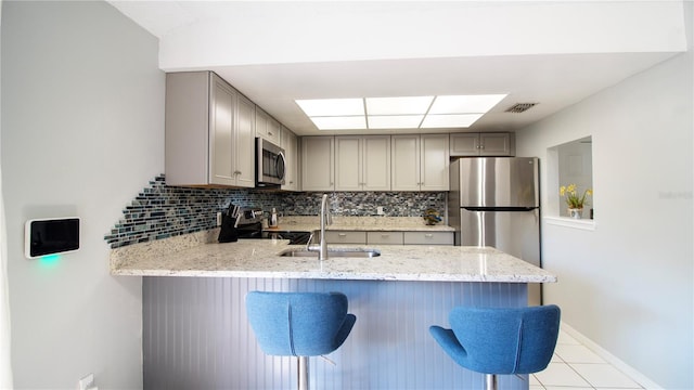 kitchen featuring decorative backsplash, stainless steel appliances, gray cabinetry, kitchen peninsula, and a breakfast bar area